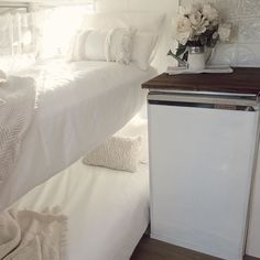 a white bed sitting under a window next to a small table with flowers on it