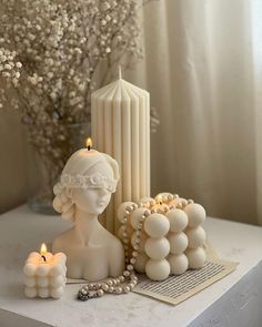 some candles are sitting on a table next to a statue and flowers in a vase