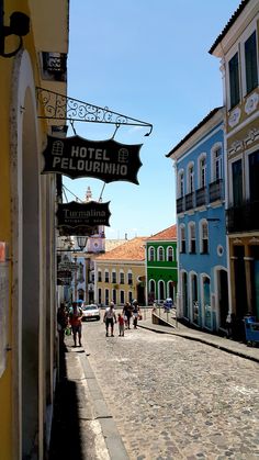 people are walking down the cobblestone street in front of colorful buildings and shops