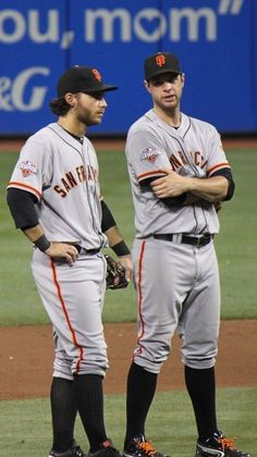 two baseball players standing on the field with their arms crossed and looking at each other