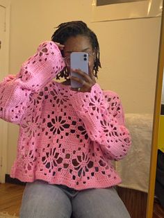 a woman taking a selfie in front of a mirror wearing a pink crocheted sweater