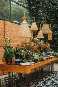 a table with plants and hanging lights in front of a brick wall on a patio