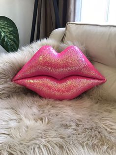 a pink glittered lip sitting on top of a white fur covered couch