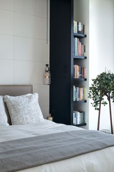 a bed with white sheets and pillows in a bedroom next to a bookshelf