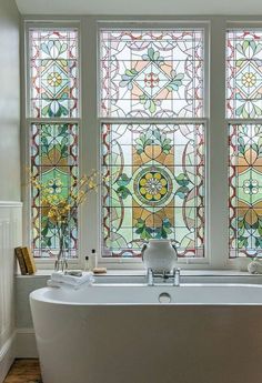 a bathtub in front of three stained glass windows with flowers on the tub side