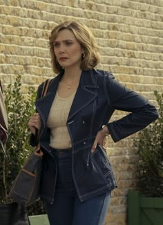 a woman standing next to a brick wall with her hands on her hips and looking at the camera