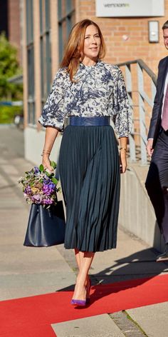 the woman is walking down the red carpet with her hand in her pocket and wearing a blue skirt