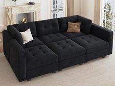 a large black couch sitting in front of a window next to a fire place with pillows on it