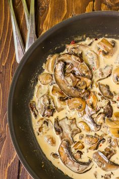 a skillet filled with mushrooms and gravy on top of a wooden table