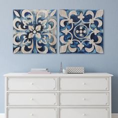 two paintings on the wall above a dresser in a room with blue walls and white furniture