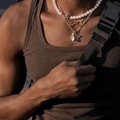 a man wearing a brown tank top holding a black guitar strap and looking at his cell phone