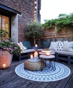 an outdoor living area with couches, tables and candles on the ground in front of a brick wall