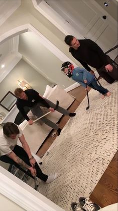 three people standing in a living room holding skis on their feet and poles,