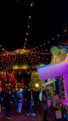 many people are walking around in the city at night with christmas lights hanging above them