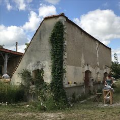 an old building with ivy growing on it's side and a woman sitting at a table outside