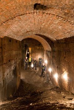 men in yellow vests and safety jackets are working on an underground tunnel with brick walls