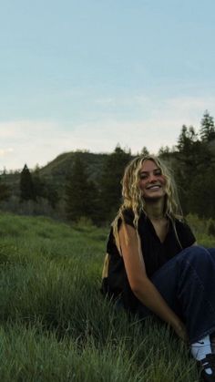 a woman sitting in the grass with her eyes closed and mouth wide open, smiling