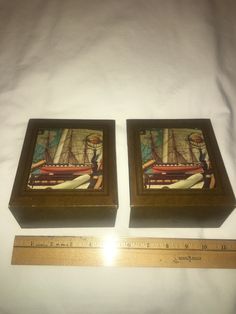 two wooden boxes with paintings on them sitting next to a ruler