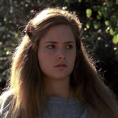 a young woman with long hair standing in front of trees and looking off into the distance