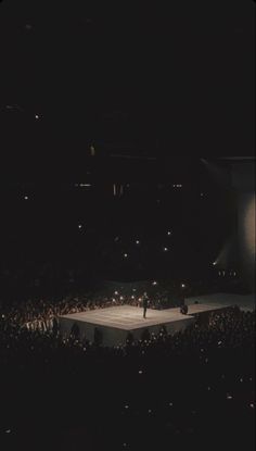 an aerial view of a stage with people on it at night, in front of a large crowd