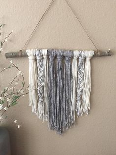 a wall hanging made from yarn and wood sticks with some flowers in the vase next to it