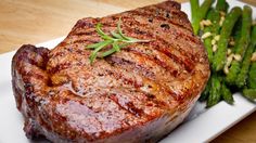 a piece of steak on a white plate with a fork and asparagus next to it