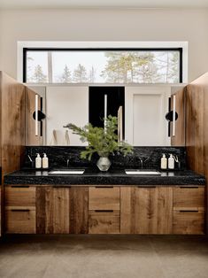 a bathroom with two sinks, mirrors and cabinets in front of a window that looks out onto the woods