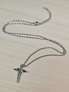 a silver chain with a bird on it sitting on a wooden table next to a cell phone