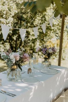 the table is set with white linens and flowers in vases on it, along with bunting