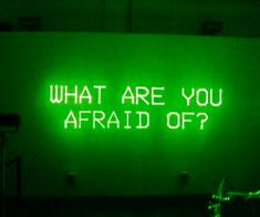 a green neon sign that says what are you afraid off? on the side of a building