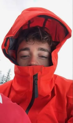 a young man wearing a red jacket and covering his face with an orange hoodie