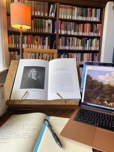 an open book sitting on top of a desk next to a laptop computer and bookshelf