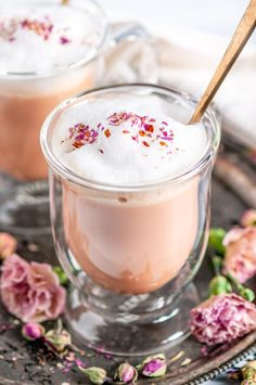 two cups filled with hot chocolate and topped with whipped cream on a plate next to pink flowers