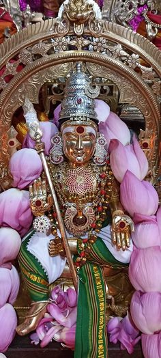 the statue is surrounded by pink flowers and other decorations, including a golden headdress