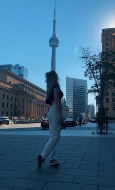 a woman riding a skateboard down a sidewalk next to tall buildings in the background