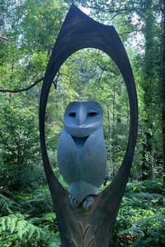 an owl statue sitting on top of a tree stump in the middle of a forest