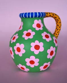 a green vase with pink and red flowers painted on the outside, sitting on a purple surface