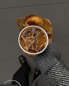 a person is holding a cup of soup and croissant