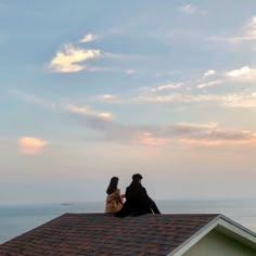 two people sitting on the roof of a house looking out at the ocean and sky