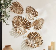 three gold leaf wall hangings on a white wall next to a vase and candles