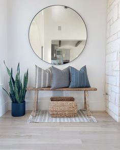 a wooden bench sitting under a round mirror next to a potted plant on top of a hard wood floor