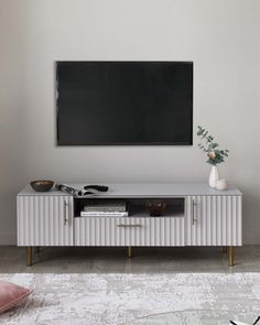 a white tv stand in front of a gray wall with a black television on it