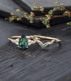 two rings with green and white stones sitting on top of a wooden table next to flowers