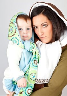 a woman holding a baby wearing a blue and green blanket on her back, while she wears a white hoodie