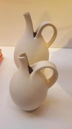 two white vases sitting next to each other on top of a table with books