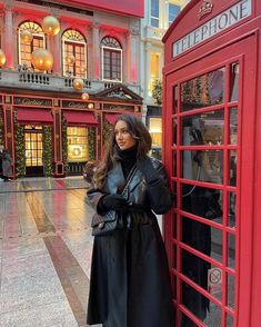 a woman standing next to a red phone booth