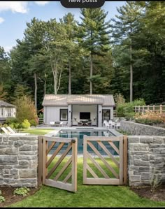 an outdoor pool surrounded by stone walls and wooden gates with a house in the background