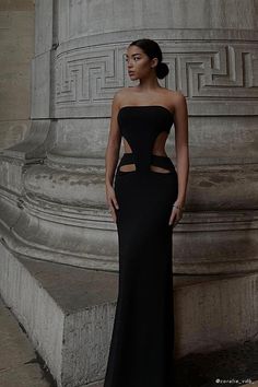 a woman standing in front of a pillar wearing a black dress with cut out sides