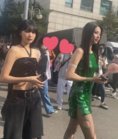 two young women dressed in costumes walking down the street with heart shaped stickers on their backs