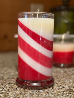 a red and white candle sitting on top of a counter next to another glass filled with liquid